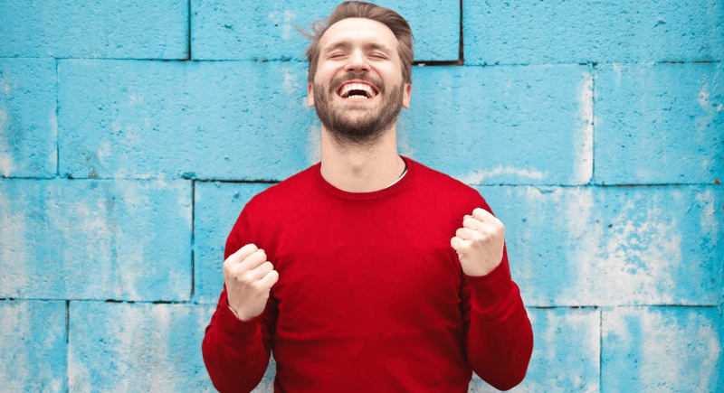 Smiling man in a red sweater against a blue brick wall